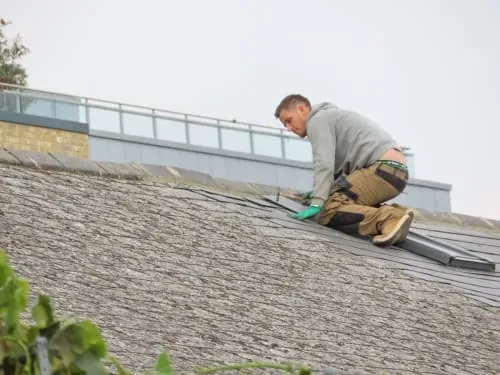A roofer repairing tiles on a pitched roof.